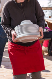 Waitress with red apron holding plate's stack, dishware