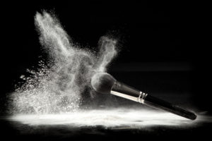 an image of a cosmetic powder brush, thrown in white loose powder, shot on black backgrownd.