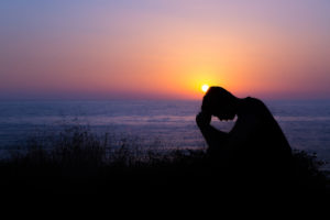 Young man praying to God during sunset by the sea