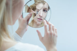 Young woman touching her own reflection in a broken mirror