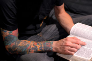 male with tattoos reading the bible